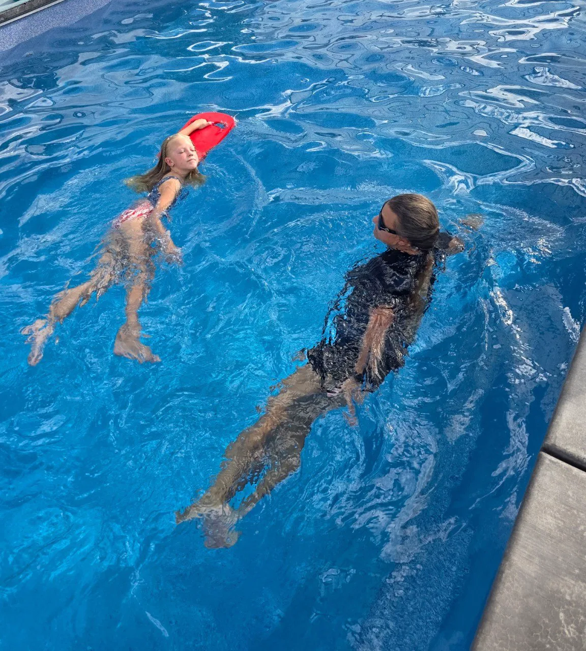 A young swimmer practicing a supported back float while the instructor stays close