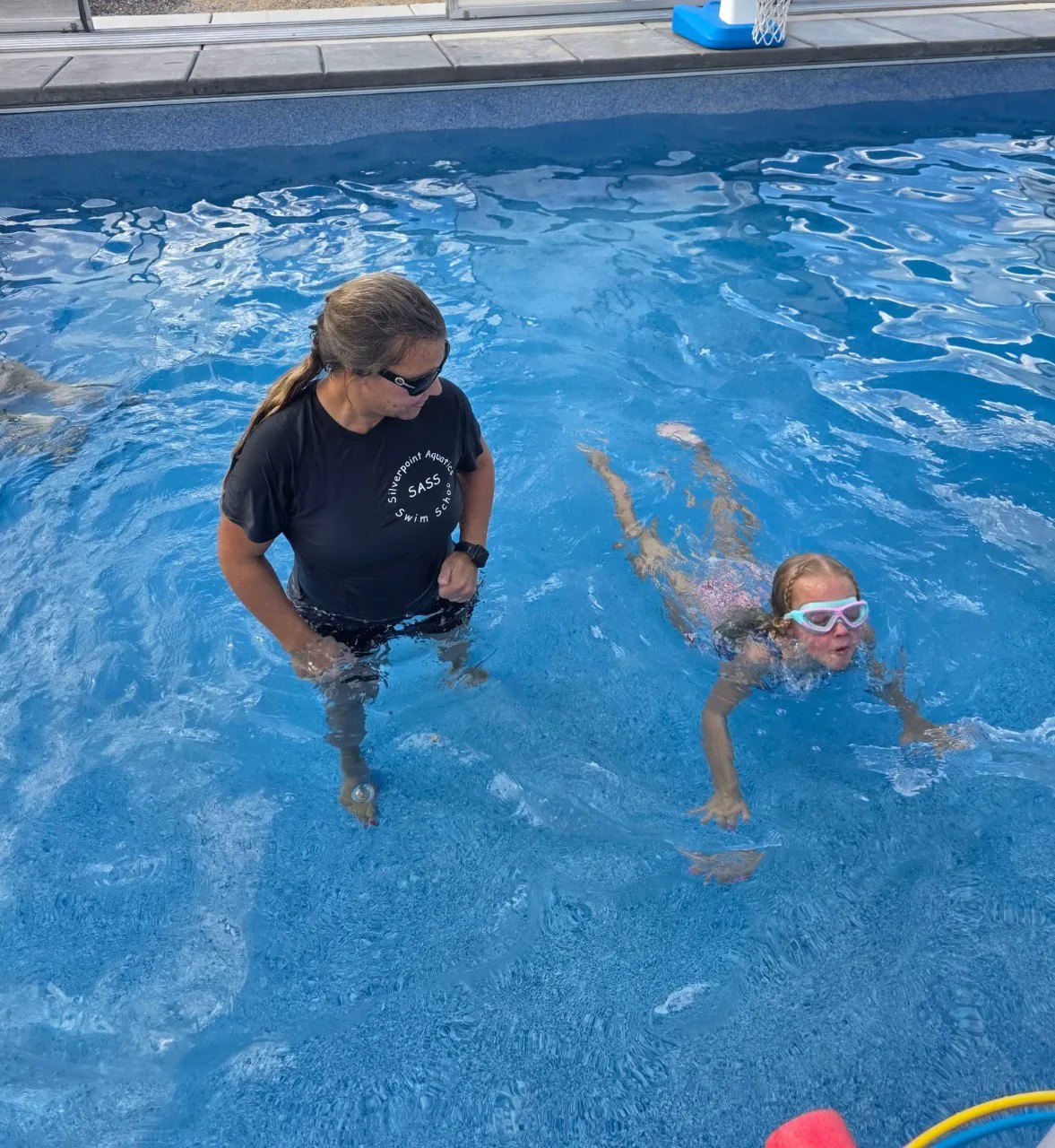 A young swimmer practicing independently while the instructor watches closely
